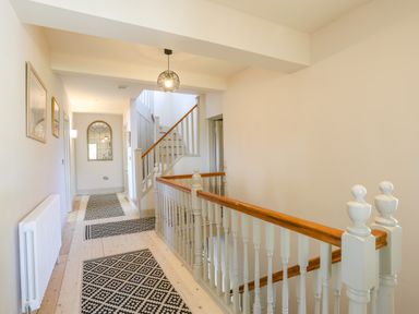 A hallway with patterned rugs on the floor and a staircase with wooden handrails at Bryn Henllan in Criccieth