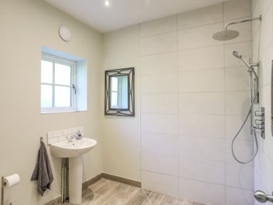 A bathroom with a pedestal sink a wall mirror a window a shower area and towels at Bryn Henllan in Criccieth