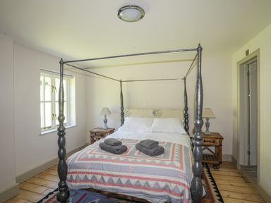 A bedroom with a four poster bed two bedside tables with lamps a window and wooden floor at Bryn Henllan in Criccieth