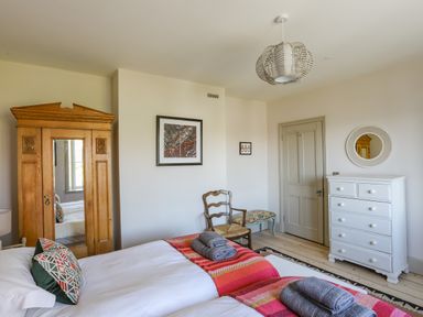 A bedroom with two beds a wooden wardrobe a white chest of drawers and a wooden chair at Bryn Henllan in Criccieth