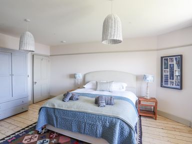 A bedroom with a bed with blue and green bedding bedside tables with lamps a wardrobe and a framed artwork on the wall at Bryn Henllan in Criccieth