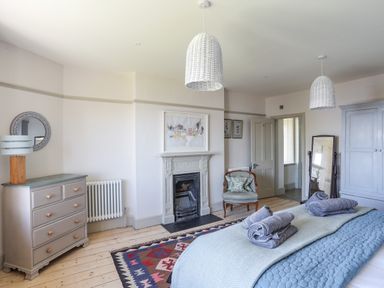 A bedroom with a bed, chest of drawers, fireplace, chair, mirror, and wardrobe at Bryn Henllan in Criccieth