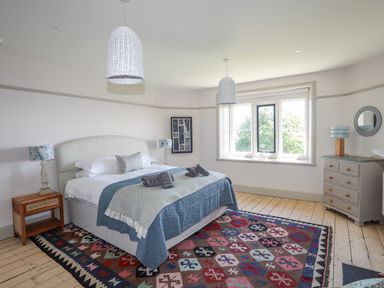 A bedroom with a bed a colorful rug a window nightstands and dresser at Bryn Henllan Criccieth