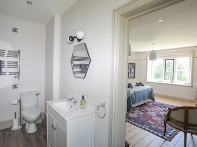 A bathroom with a toilet and sink next to a bedroom with a bed and patterned rug at Bryn Henllan in Criccieth