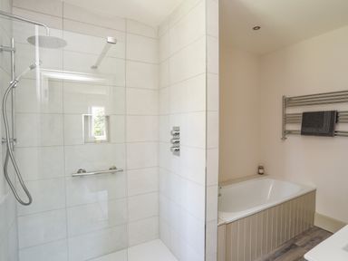 A bathroom with a glass shower enclosure and a bathtub with a towel rack above at Bryn Henllan Criccieth