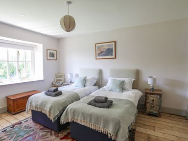 A bedroom with two single beds bedside tables a window and a wooden chest at Bryn Henllan in Criccieth