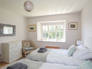 A bedroom with two single beds a wicker chair a white chest of drawers and a window at Bryn Henllan in Criccieth