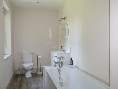 A bathroom with a toilet bathtub sink mirror and window at Bryn Henllan in Criccieth