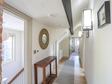 A hallway with a wooden table a round mirror and framed pictures at Bryn Henllan in Criccieth