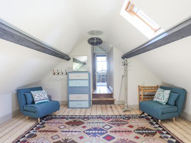 An attic room with two blue chairs a multicolored rug chest of drawers a mirror coat rack and a skylight at Bryn Henllan in Criccieth