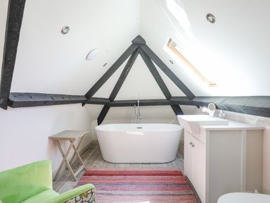 A bathroom with a freestanding bathtub under a sloped ceiling with black beams a sink with cabinet and a skylight window at Bryn Henllan in Criccieth