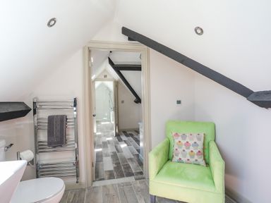 A small room with a green chair and cupcake cushion a heated towel rack and a doorway leading to a bathroom at Bryn Henllan in Criccieth