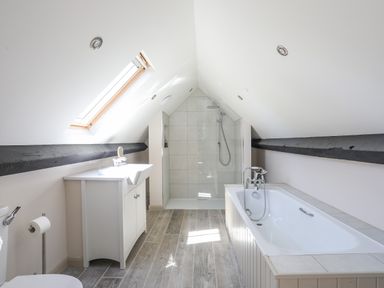A bathroom with a bathtub sink and shower under a slanted ceiling with a skylight at Bryn Henllan in Criccieth