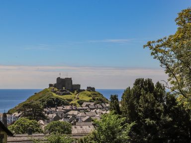 A hill with castle ruins overlooking a town and the sea with trees in the foreground at Bryn Henllan in Criccieth