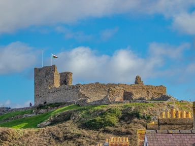 A stone castle ruin on a hill with a flag flying against a blue sky at Bryn Henllan in Criccieth