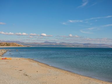 A sandy beach with a kayak on the shore and a calm sea with hills in the background at Bryn Henllan in Criccieth