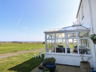 A glass conservatory attached to a white house with potted plants outside and a grassy field in the background at Trewan House Bryngwran near Rhosneigr Rhosneigr