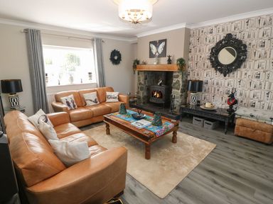 A living room with two leather sofas a wooden coffee table a stone fireplace and decorative wallpaper at Trewan House Bryngwran near Rhosneigr Rhosneigr