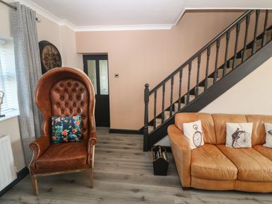 A living room with a brown leather armchair a tan leather sofa and black staircase at Trewan House Bryngwran near Rhosneigr Rhosneigr