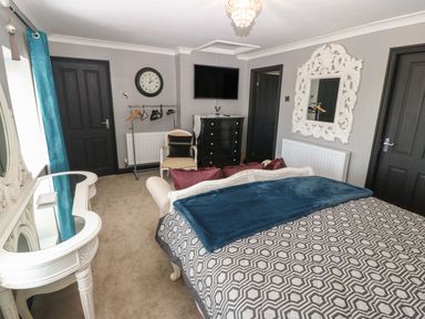 A bedroom with a bed a chair a dresser a wall clock a TV and a mirror at Trewan House Bryngwran near Rhosneigr Rhosneigr