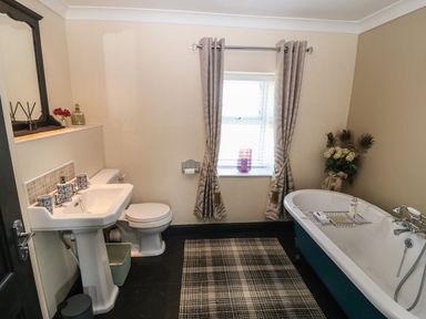 A bathroom with a sink and toilet on the left and a bathtub with flowers on the right at Trewan House in Bryngwran near Rhosneigr Rhosneigr