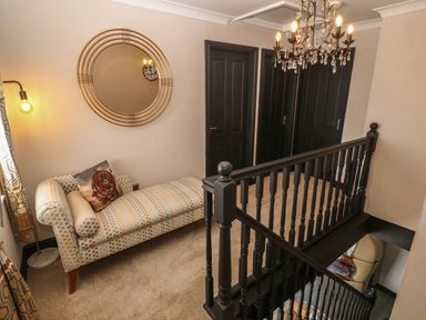 An upstairs landing with a patterned chaise lounge round mirror on wall black doors and railing at Trewan House Bryngwran near Rhosneigr Rhosneigr