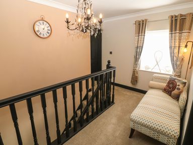 A staircase landing with a patterned chaise lounge near a window with curtains and a chandelier hanging from the ceiling at Trewan House in Bryngwran near Rhosneigr Rhosneigr