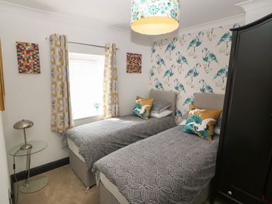 A bedroom with two single beds a black wardrobe a glass lamp table and a window with patterned curtains at Trewan House Bryngwran near Rhosneigr Rhosneigr