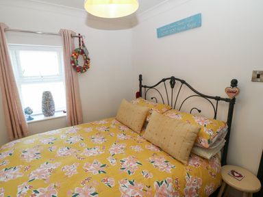 A bedroom with a bed with floral yellow bedding and pillows next to a window with pink curtains at Trewan House Bryngwran near Rhosneigr Rhosneigr