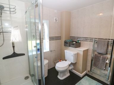 A bathroom with a shower enclosure a toilet a window towel rack and storage baskets at Trewan House Bryngwran near Rhosneigr Rhosneigr