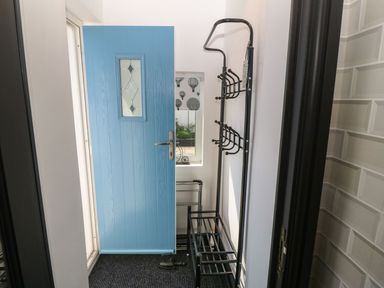 A small entryway with a blue door a black metal coat rack and a window with patterned curtains at Trewan House in Bryngwran near Rhosneigr Rhosneigr