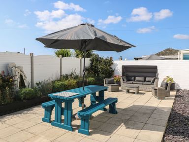 An outdoor patio area with a blue picnic table and umbrella and grey cushioned wicker furniture at Trewan House Bryngwran near Rhosneigr Rhosneigr