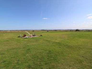 A large green field with scattered garden sculptures and a fence in the background at Trewan House Bryngwran near Rhosneigr Rhosneigr