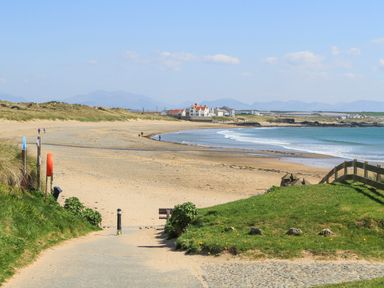 A sandy beach with a pathway leading to the shore and houses in the distance at Trewan Lodge in Bryngwran near Rhosneigr