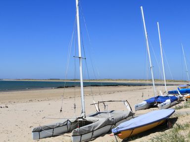 A sandy beach with several small sailboats lined up near the shore at Trewan Lodge in Bryngwran near Rhosneigr