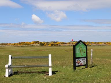 A golf course hole marker with a bench and a red flag on the green at Trewan Lodge in Bryngwran near Rhosneigr