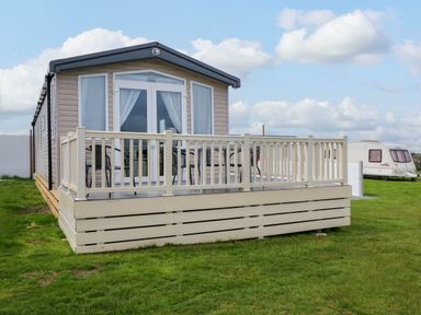 A mobile home with a deck and railing on grass with another caravan in the background at Trewan Lodge in Bryngwran near Rhosneigr