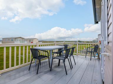 A deck with a table and four chairs overlooking grassy land and mobile homes at Trewan Lodge in Bryngwran near Rhosneigr