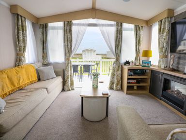 A living room with sofas a coffee table a fireplace and a TV with outside view at Trewan Lodge in Bryngwran near Rhosneigr