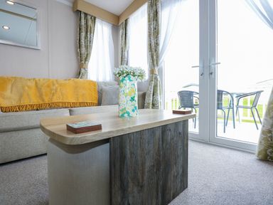 A living room with a wooden coffee table with a flower vase on it and a sofa with a yellow throw at Trewan Lodge in Bryngwran near Rhosneigr