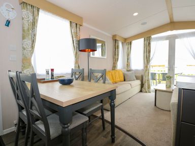 A dining area with a wooden table and four chairs next to a living room with a beige sofa and a coffee table at Trewan Lodge in Bryngwran near Rhosneigr