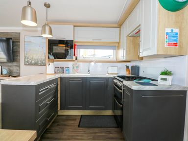 A kitchen with dark lower cabinets white upper cabinets a microwave stove toaster sink and hanging lights at Trewan Lodge in Bryngwran near Rhosneigr