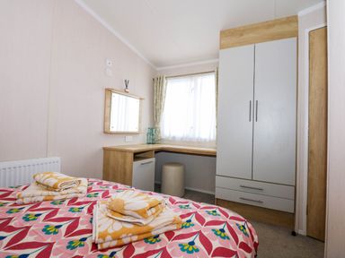 A bedroom with a bed, a wardrobe, a desk with a stool, and a window at Trewan Lodge in Bryngwran near Rhosneigr