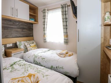 A bedroom with two single beds floral bedding a window with check curtains and a wardrobe at Trewan Lodge in Bryngwran near Rhosneigr