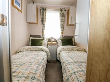 A bedroom with two single beds a small nightstand and a window with curtains at Trewan Lodge in Bryngwran near Rhosneigr