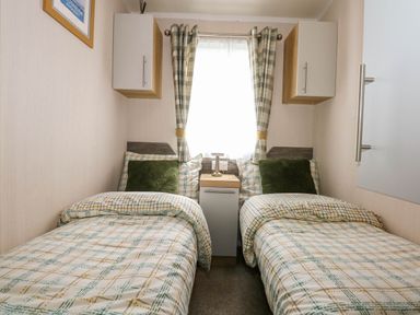 A bedroom with two single beds a window with curtains and a bedside table at Trewan Lodge Bryngwran near Rhosneigr