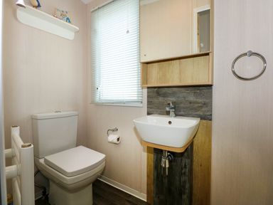 A bathroom with a toilet roll holder a window with blinds a small sink and a mirror cabinet at Trewan Lodge in Bryngwran near Rhosneigr