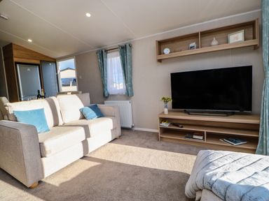 A living room with a beige sofa blue cushions a television on a wooden stand and blue curtains at Wansbeck View 2 in Ashington
