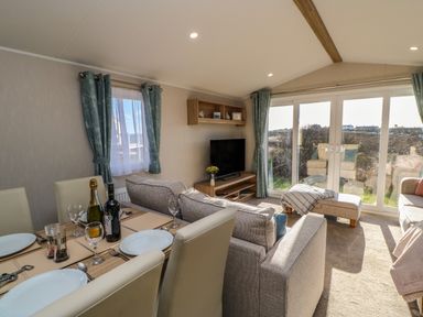 A living and dining area with a dining table set with plates and glasses next to sofas and a television at Wansbeck View 2 in Ashington