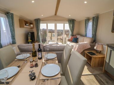 A dining table set with plates glasses cutlery and bottles next to a living room with sofas cushions and a television at Wansbeck View 2 in Ashington